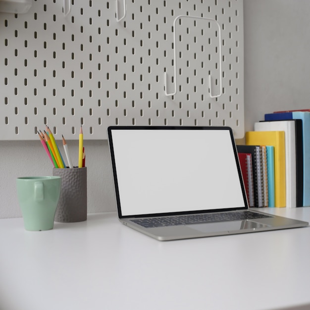 Stijlvolle kantoor aan huis met een leeg scherm laptop, mok, briefpapier en boeken op witte tafel