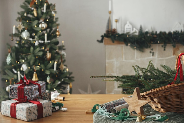 Stijlvolle kerstcadeaus en feestelijke decoraties op tafel op achtergrond van een prachtige vintage kerstboom en open haard Vrolijk kerstfeest en gelukkige feestdagen Voorbereiding voor de winterfeesten