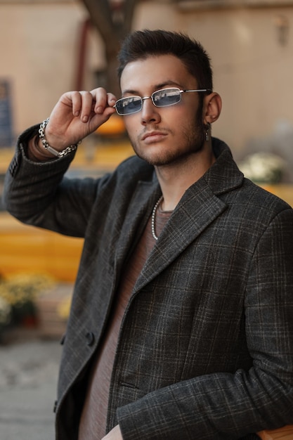 Stijlvolle knappe jonge succesvolle zakenman model man in modieuze kleding met jas met vintage zonnebril op straat