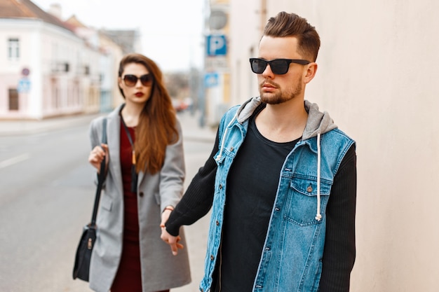 Stijlvolle knappe man in jeans kleding en zonnebril met een vriendin op straat