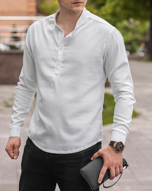 Stijlvolle knappe modelman in vrijetijdskleding op straat met horloge en leren clutch