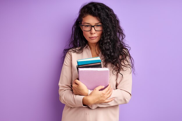 Stijlvolle leraar in bril poseren bedrijf boeken in handen geïsoleerd over paarse muur