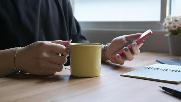 Stijlvolle man hand met koffiekopje en het gebruik van mobiele telefoon op houten tafel