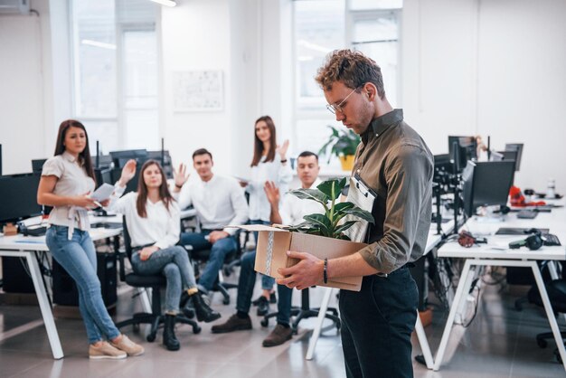 Stijlvolle man in bril met doos met plant voor zijn collega's op kantoor.