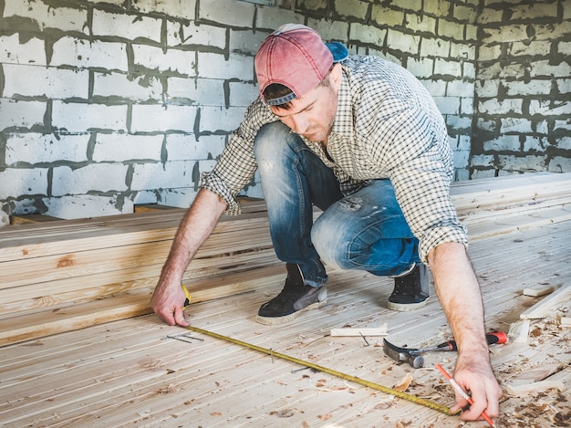 Stijlvolle man in een baseballpet, spijkerbroek en een shirt, werkt met gereedschap op hout in het huis in aanbouw. Concept van constructie en reparatie