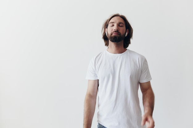 Stijlvolle man in een wit t-shirt met draadloze koptelefoon in zijn oren die plezier hebben met het luisteren naar muziek glimlach op een witte achtergrond levensstijl