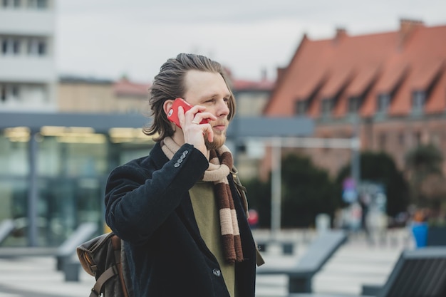 Stijlvolle man in sjaal en jas praten via de mobiele telefoon in de straat van Wroclaw, Polen