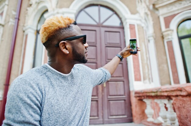 Stijlvolle man op grijze trui en zwarte zonnebril poseerde op straat Modieuze zwarte man selfie maken op telefoon.