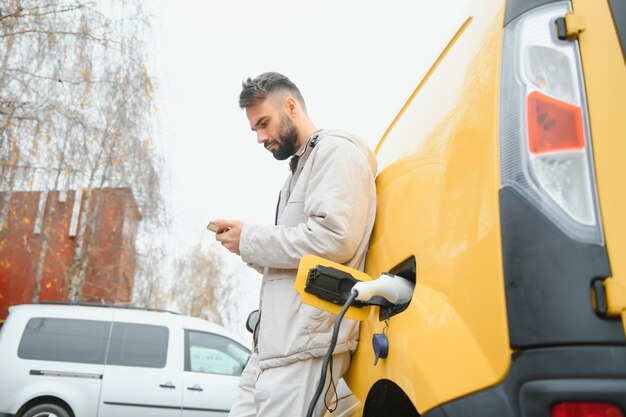 Stijlvolle man steekt de oplaadkabel in het stopcontact van de elektrische auto