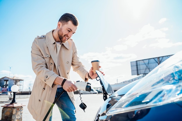 Stijlvolle man steekt stekker in de oplaadaansluiting van de elektrische auto