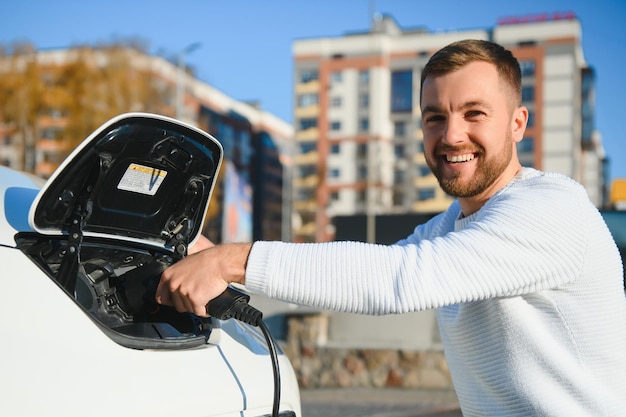 Stijlvolle man steekt stekker in de oplaadaansluiting van de elektrische auto