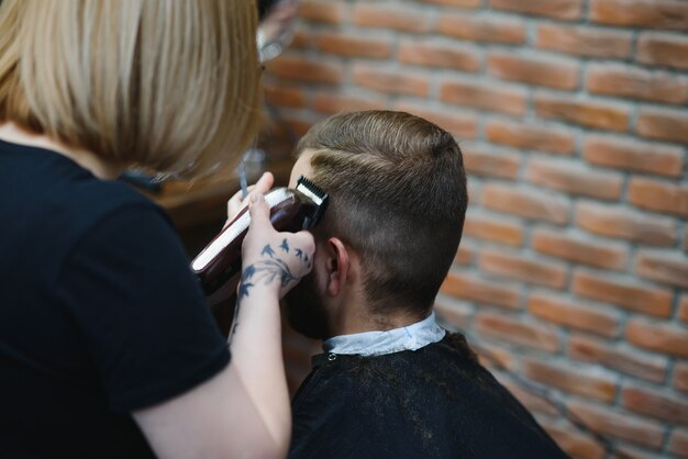 Foto stijlvolle man zit kapper haarstylist kapper portret knappe gelukkig jonge bebaarde blanke man trendy kapsel krijgen aantrekkelijke kapper meisje werken serveren klant