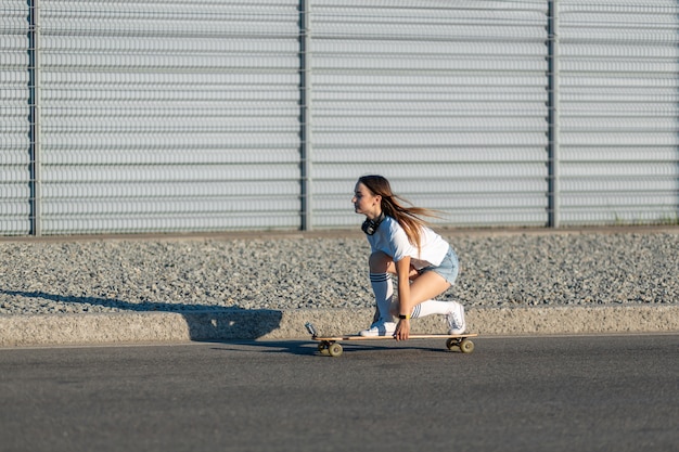 Stijlvolle meisje in witte kousen rijden op longboard in de straat en muziek luisteren