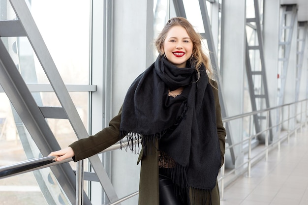 Stijlvolle mode portret van blonde vrouw poseren in de stad Mooi meisje in herfst groene jas en zwarte sjaal poses in een overhead voetgangersoversteekplaats