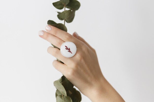 Stijlvolle moderne witte ronde ring aan mooie hand met eucalyptustak op witte achtergrond