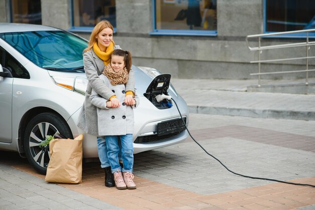 Stijlvolle moeder en dochter laden een elektrische auto op en brengen samen tijd door