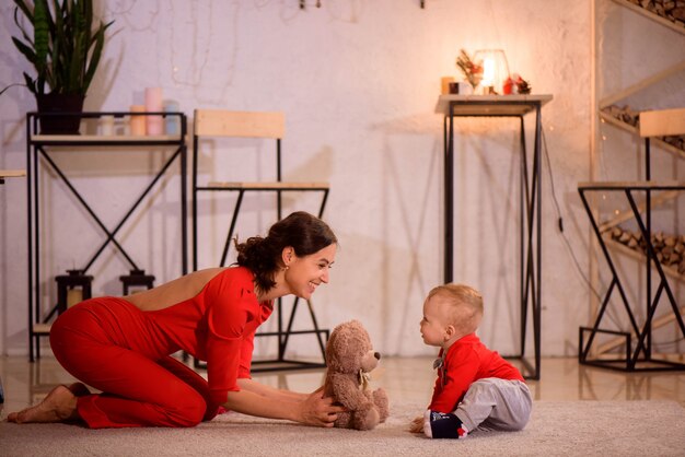 Stijlvolle moeder spelen met baby boy zittend op de vloer in de buurt van kerstversiering