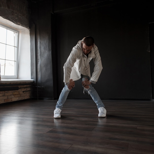 Stijlvolle mooie hiphop danseres in modieuze kleding met blauwe gescheurde spijkerbroek met sneakers dansen in een donkere dansstudio