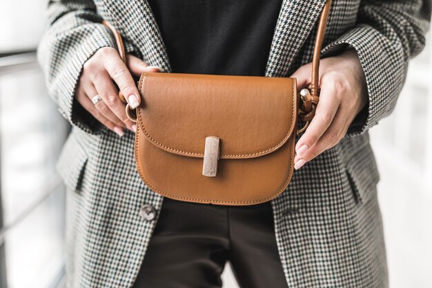 Stijlvolle mooie jonge vrouw in elegante kleding met een bruine leren handtas aan een riem