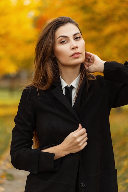 Stijlvolle mooie jonge vrouw in modieuze kleding en stropdas wandelen in een herfst gekleurd park