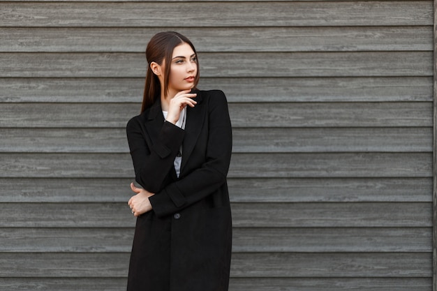 Stijlvolle mooie model vrouw in zwarte jas poseren in de buurt van vintage houten huis