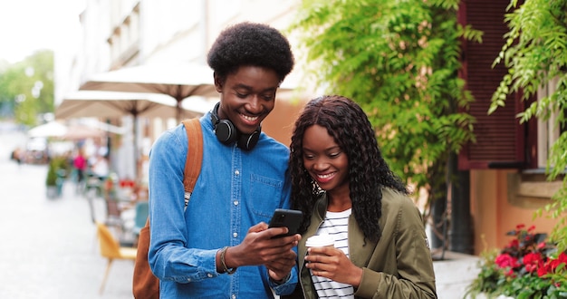 Stijlvolle multiraciale man en zijn vriendin gebruiken zijn smartphone terwijl ze handso...