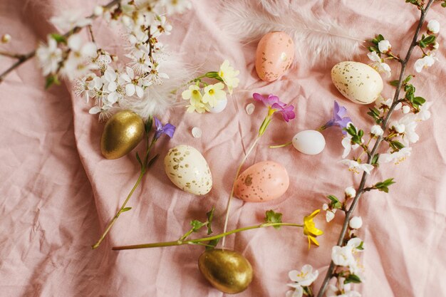 Stijlvolle paaseieren en bloeiende lentebloemen op roze linnen stof Happy Easter Moderne eieren veren en kersenbloesems Rustiek paasstilleven