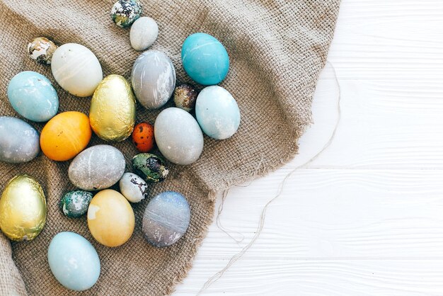 Stijlvolle paaseieren op rustieke stof op witte houten achtergrond plat leggen met ruimte voor tekst Moderne kleurrijke paaseieren geschilderd met natuurlijke kleurstof Happy Easter wenskaart