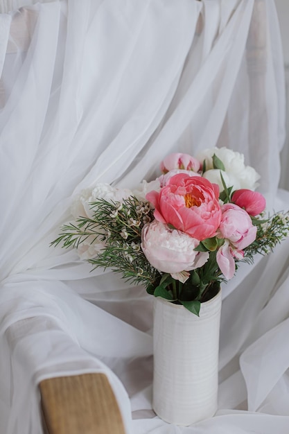 Stijlvolle pioenrozen boeket op achtergrond van zachte witte stof bloemen in keramische vaas Moederdag