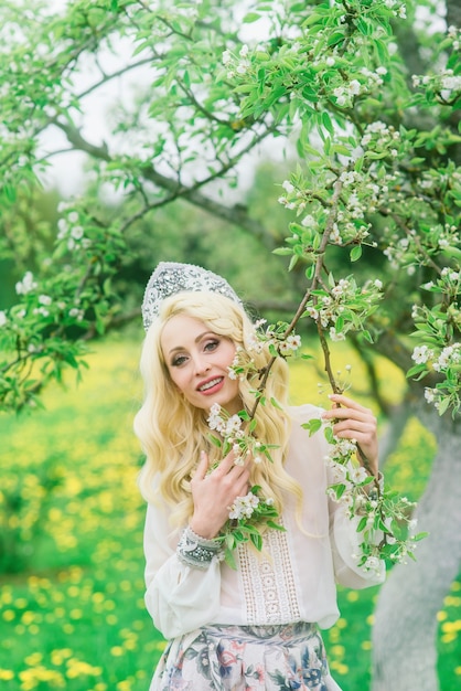 Stijlvolle Russische vrouw in traditionele nationale volkskleding, Slavische hoofdtooi, witte lentebloemen.