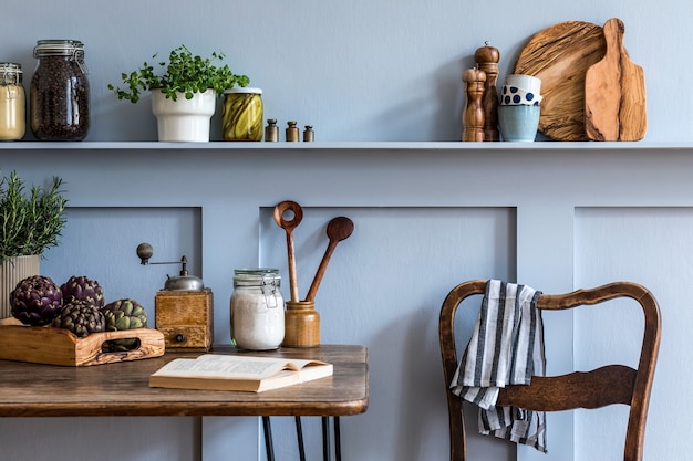 Stijlvolle samenstelling van keukeninterieur met houten familietafel, stoelen, groenten, kruiden, planten, fruit, voedselbenodigdheden en keukentoebehoren in grijs concept van huisdecor.