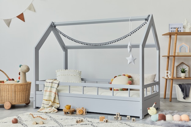 Stijlvolle scandinavische kinderkamer met creatief houten bed, rotanmand, houten plank, pluche en houten speelgoed en hangende textieldecoraties. grijze muren, tapijt op de vloer. sjabloon.