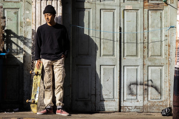 Stijlvolle skateboarder in straat met casual kleding poseren met een longboard in zijn handen