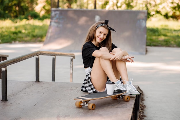 Stijlvolle tienermeisje met skateboard zitten en chillen in het skaterspark