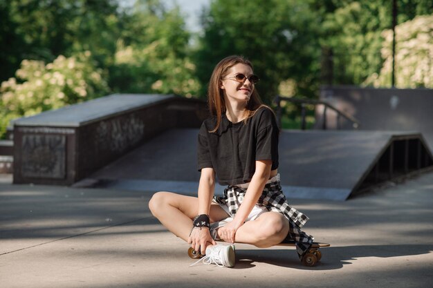 Stijlvolle tienermeisje met skateboard zitten en chillen in het skaterspark