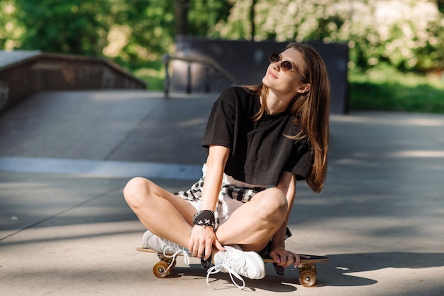 Stijlvolle tienermeisje met skateboard zitten en chillen in het skaterspark