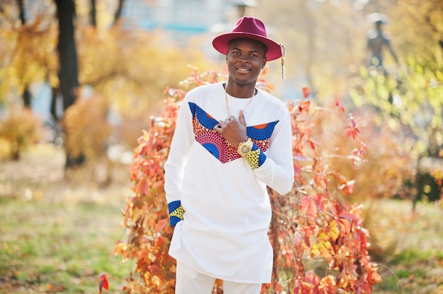 Stijlvolle trendy afro frankrijk man in rode hoed en witte outfit gesteld op herfstdag. Zwarte Afrikaanse model man.