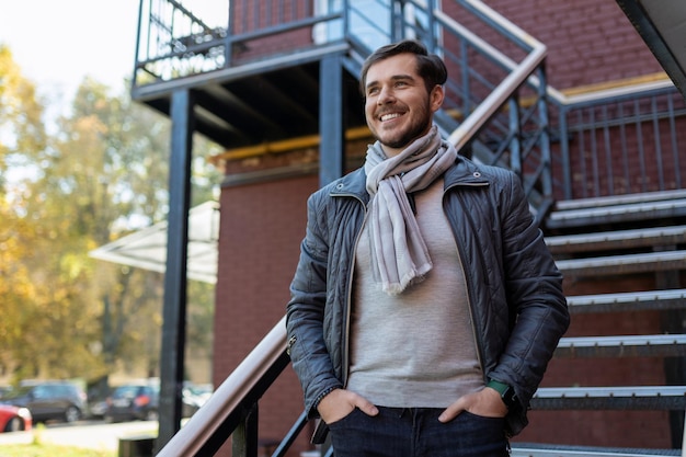 Stijlvolle volwassen man met een brede glimlach staat en kijkt naar de straat