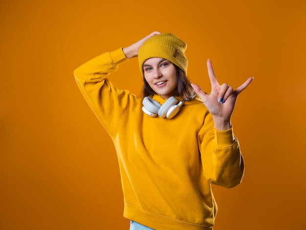 Stijlvolle vrolijke jonge brunette in een gele hoodie en hoeden toont een cool gebaar twee vingers op een...
