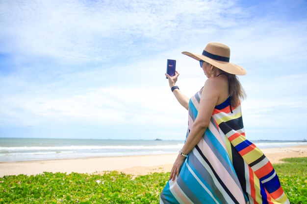 Stijlvolle vrouw draagt een kleurrijke lange jurk Sta in de zon aan de kust en kijk naar het prachtige natuurlijke landschap. Toeristische zee strand Thailand, Azië, zomervakantie vakantie reizen reis.