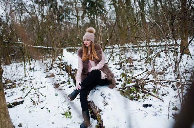 Stijlvolle vrouw in bontjas en hoofddeksels in winter forest.