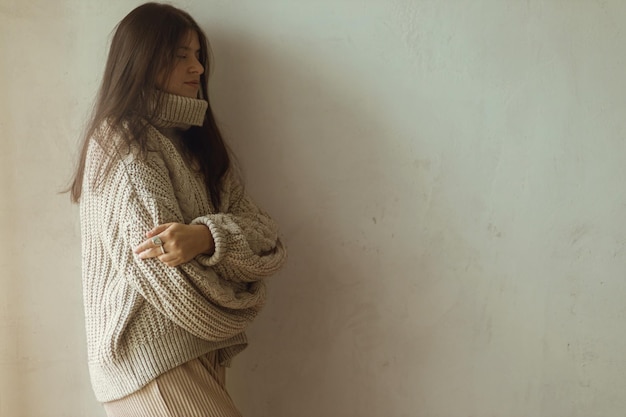 Stijlvolle vrouw in een gezellige gebreide trui die poseert op de achtergrond van een rustieke muur Gezellige herfstkleding Modieuze vrouw in neutrale beige warme doek humeurige herfst esthetiek kopieerruimte