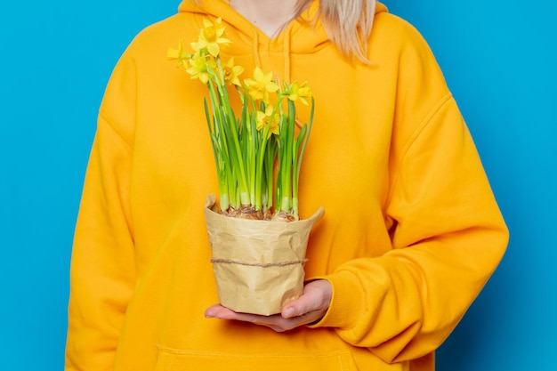 Stijlvolle vrouw in gele hoodie met narcissen bloemen op blauwe achtergrond