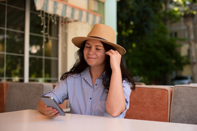 Stijlvolle vrouw in hoed met smartphone outsidemaking videogesprek