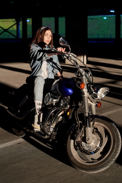 stijlvolle vrouw in spijkerbroek zittend op een motorfiets geparkeerd in de buurt van een winkelcentrum.