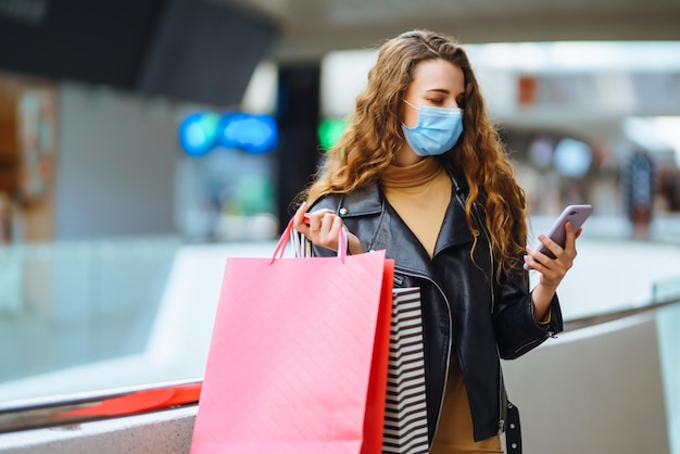 Stijlvolle vrouw met beschermend medisch masker met boodschappentassen die haar telefoon gebruikt Modestijl