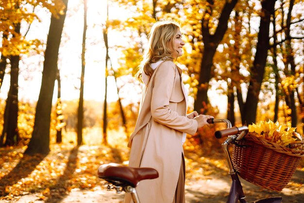 Stijlvolle vrouw met fiets die geniet van het herfstweer in het park Mooie vrouw in het herfstbos