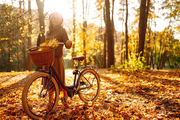 Stijlvolle vrouw met fiets genieten van herfstweer in het park Mooie vrouw in het herfstbos
