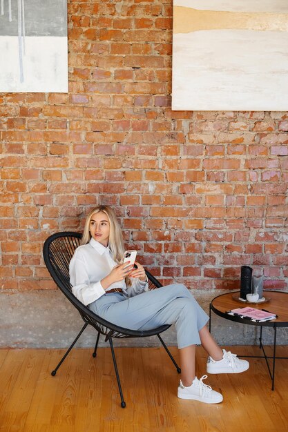 Foto stijlvolle vrouw zit op kantoor met een bakstenen muur