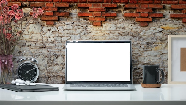 Stijlvolle werkplek met laptopcomputer koffiekopje en briefpapier op witte tafel tegen bakstenen muur Leeg scherm voor uw reclametekst